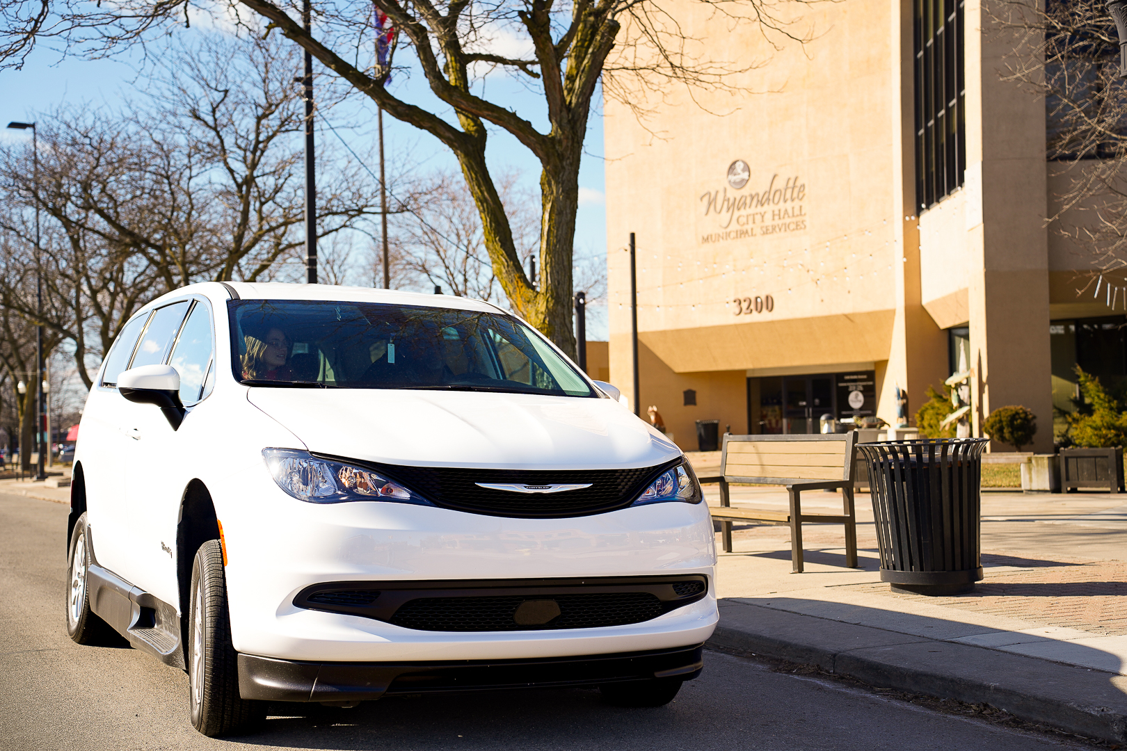 White minivan parked on a street near a city building and benches.