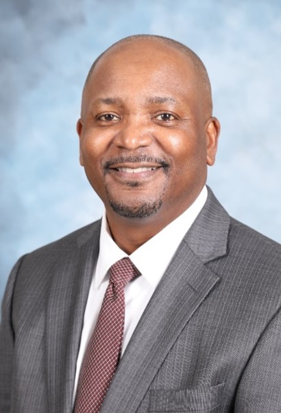 Smiling man in a suit and tie against a light blue background.