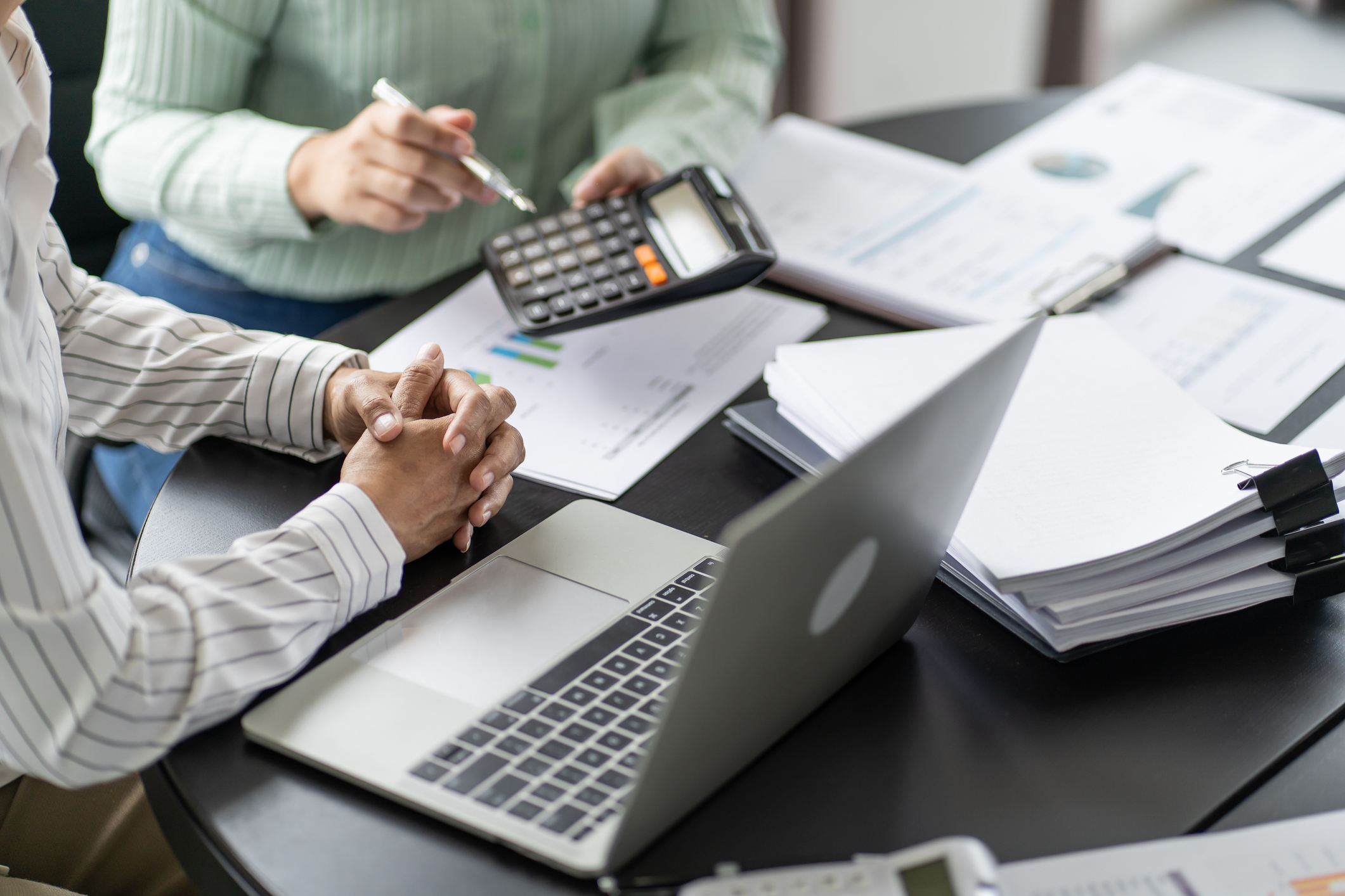 Two people review financial documents with a laptop and calculator at a desk.