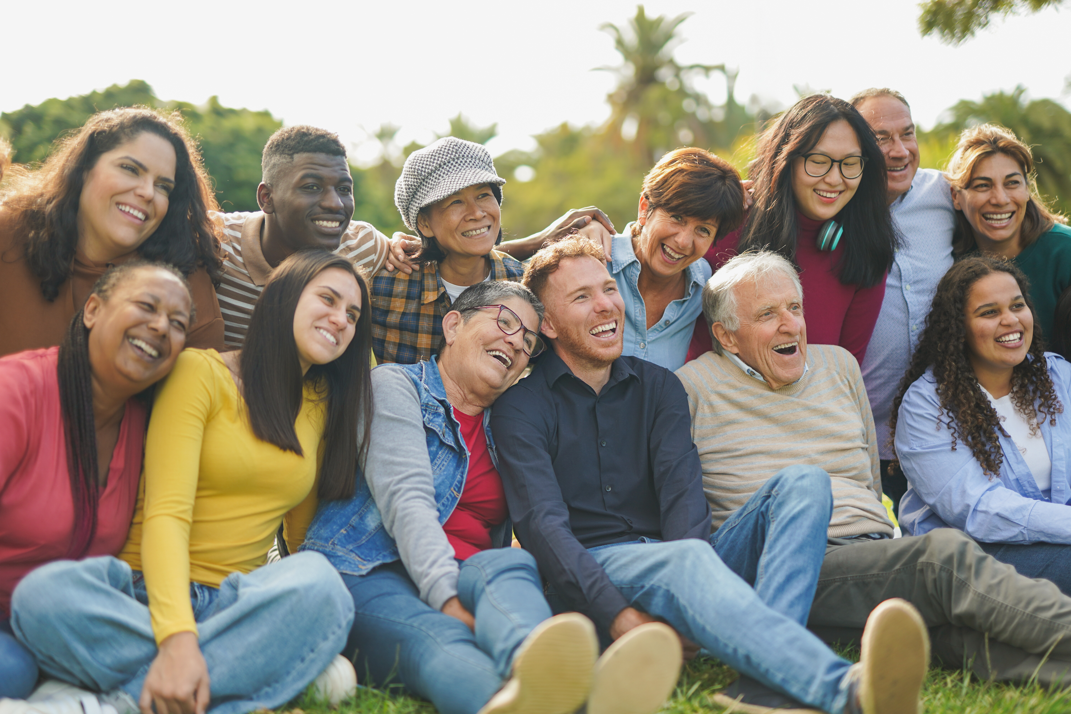 Diverse group of people sitting on grass, smiling and laughing together outdoors.