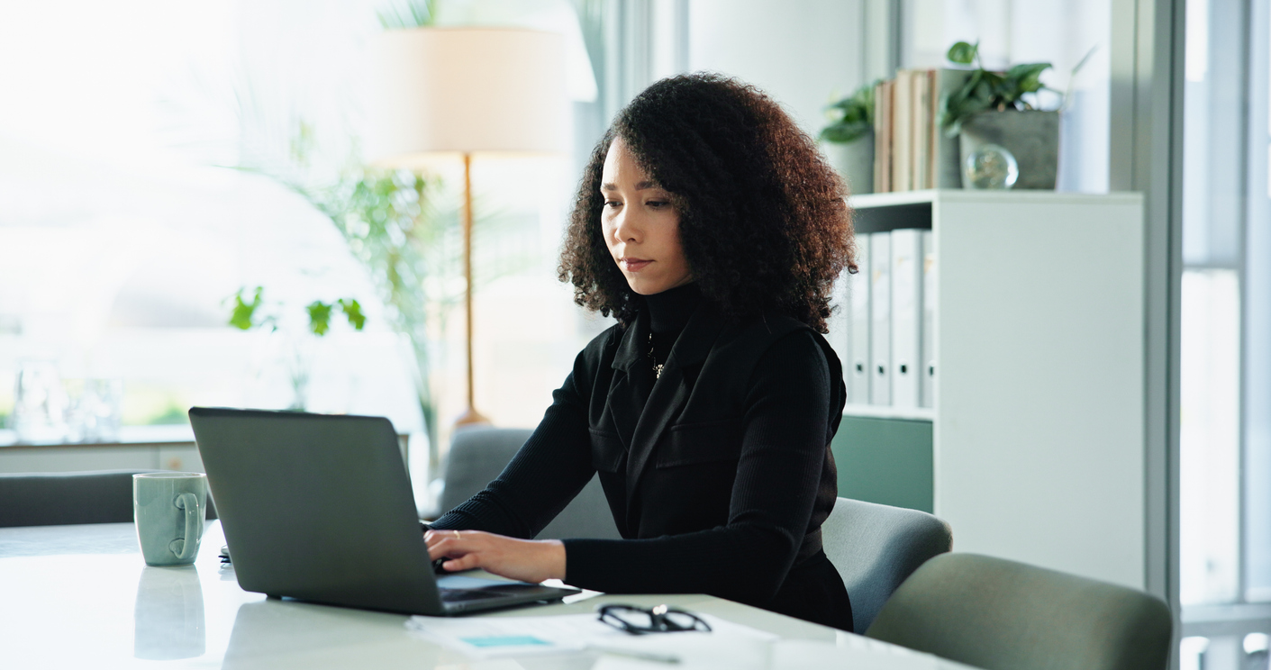 Woman working on a laptop at a desk in a bright, modern office.