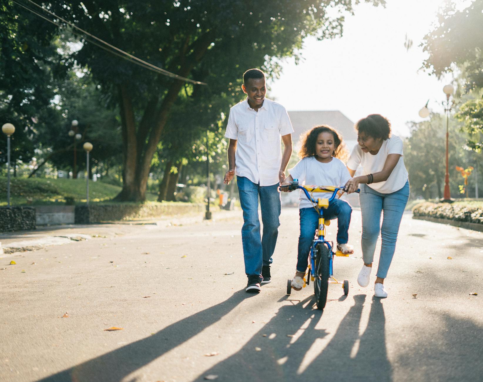 Parents helping their daughter learn to ride on a sunny path in a park