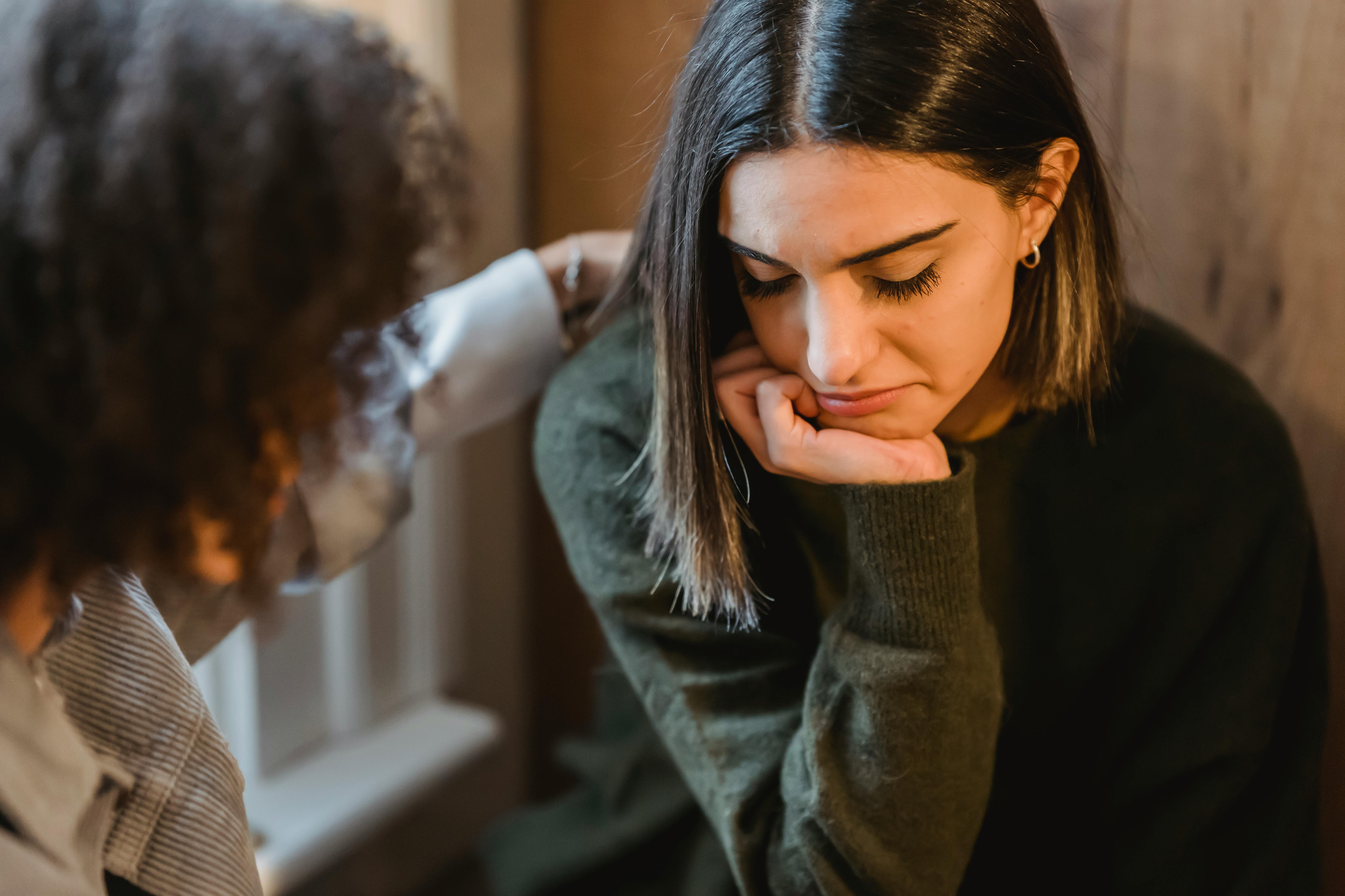 Woman looking sad while another person comforts her with a hand on her shoulder.