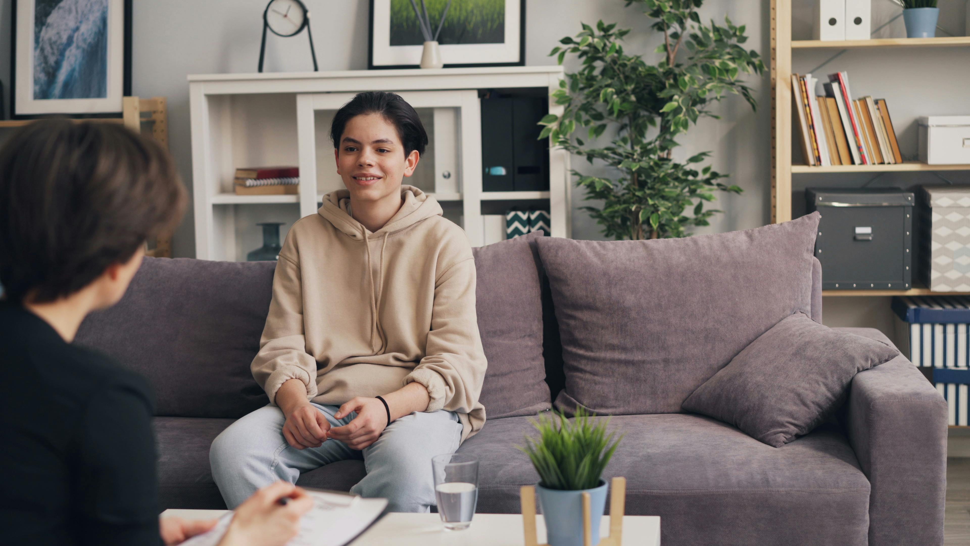 Teenager smiling on a couch during a therapy session in a cozy office.