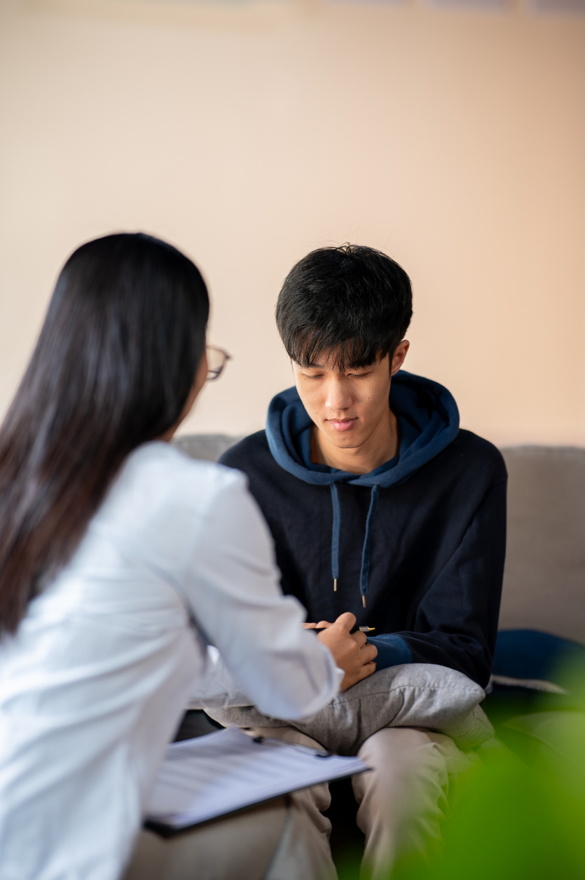 Teen boy sitting with a counselor who offers support by holding his hand.
