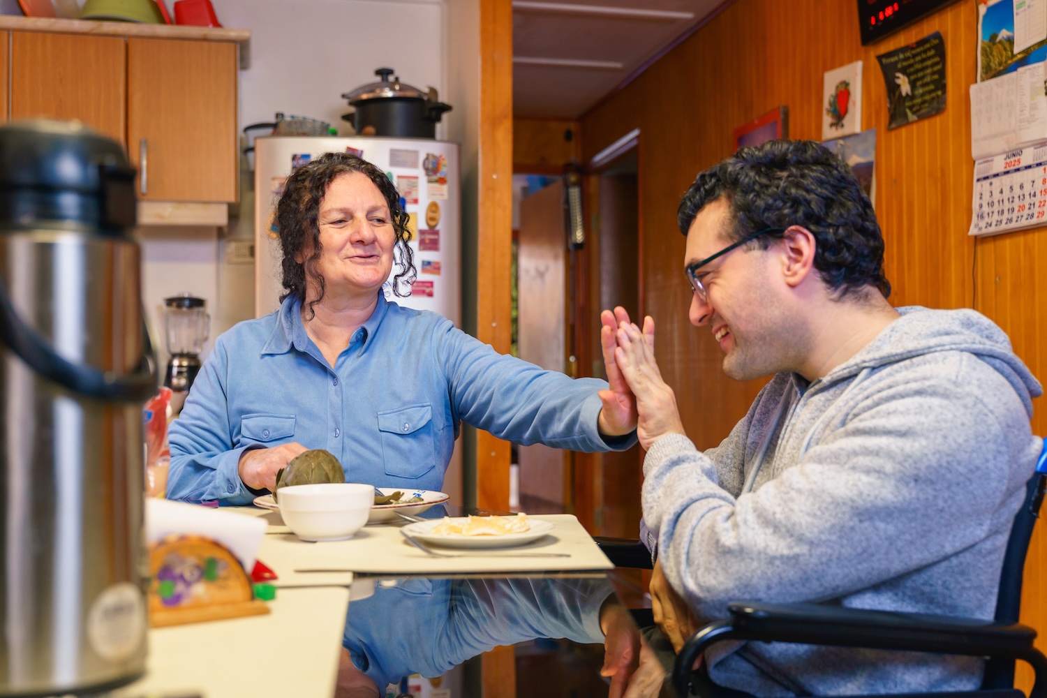 Two people smiling and giving a high-five at a kitchen table.