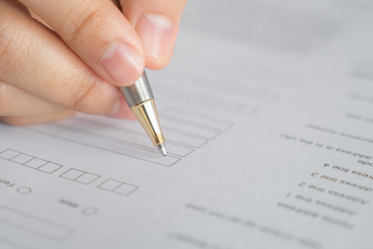 Hand holding a pen, filling out a form with boxes and printed questions.
