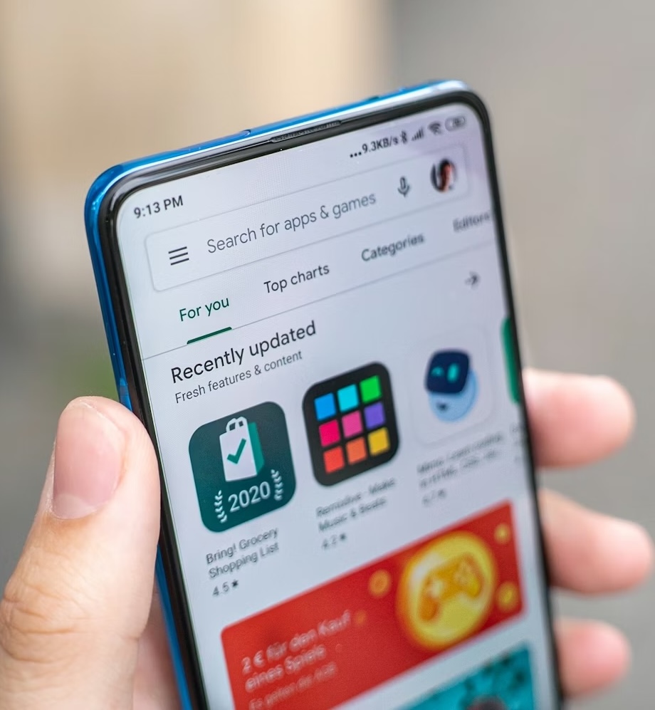 Hand holding a smartphone displaying the Google Play Store app.