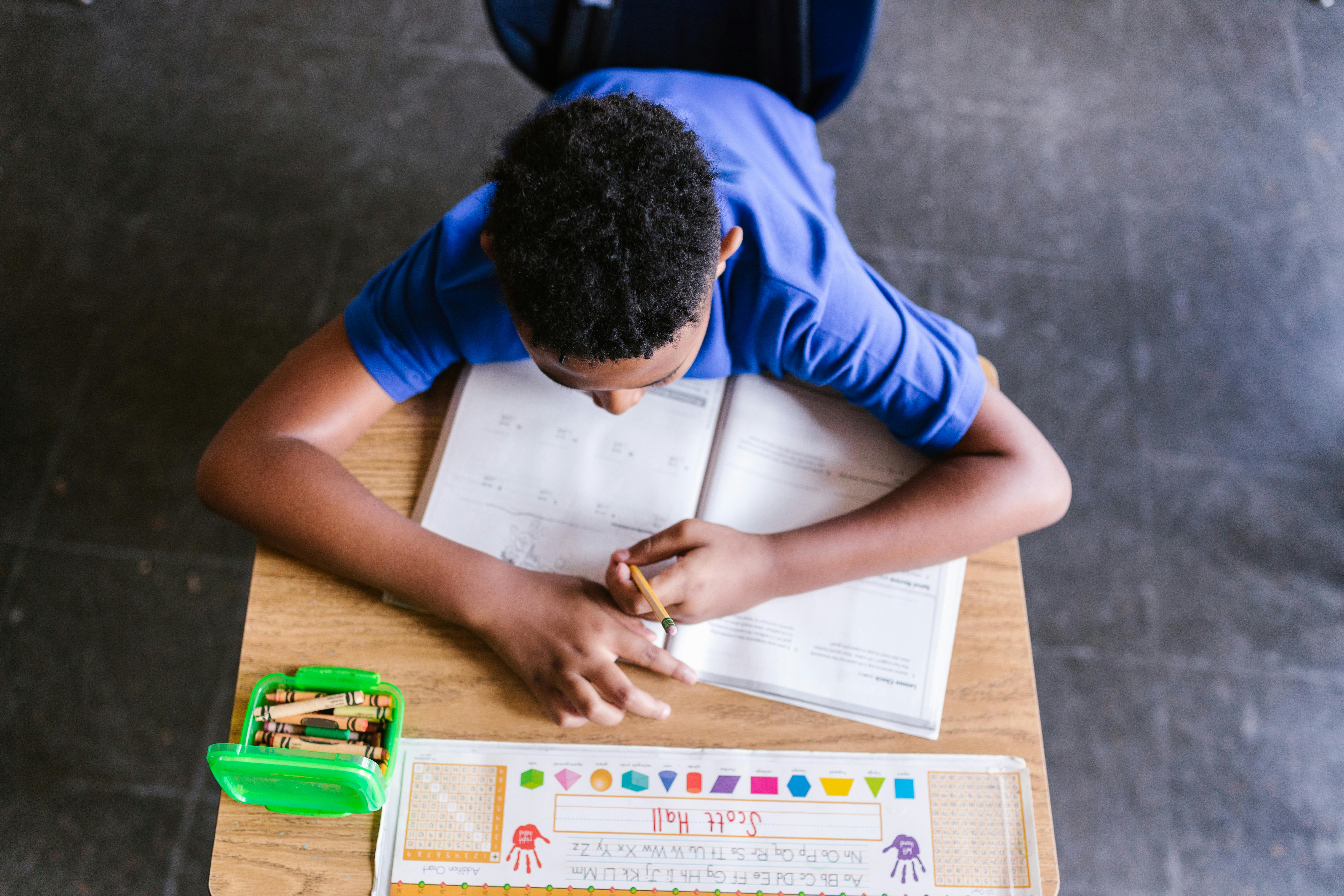 A student sitting at his desk writing in his workbook.