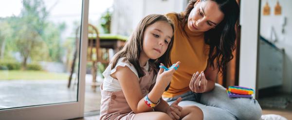 Woman and young girl sitting on the floor painting together near a large window.