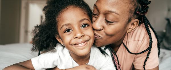 Woman kissing smiling child on the cheek while lying on a bed.
