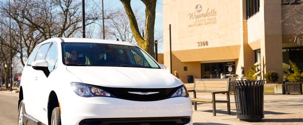 White minivan parked on a street near a city building and benches.