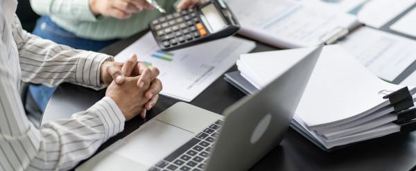 Two people review financial documents with a laptop and calculator at a desk.
