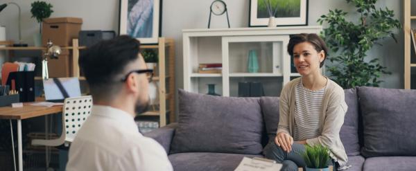 Woman sitting on a couch talking to a therapist in a modern office.