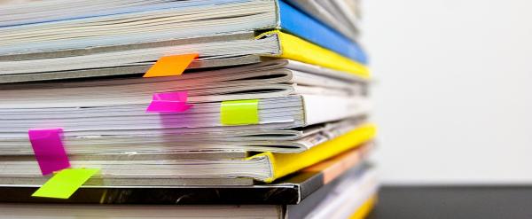 Stack of books and paperwork marked with colorful sticky tabs on a black surface.