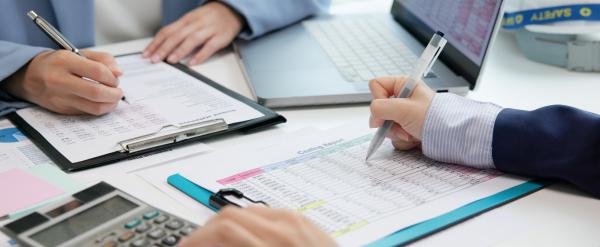 Two people review financial documents with a calculator and laptop on a desk.