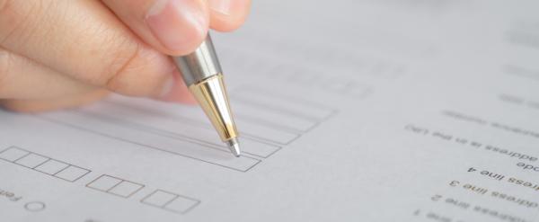 Hand holding a pen, filling out a form with boxes and printed questions.