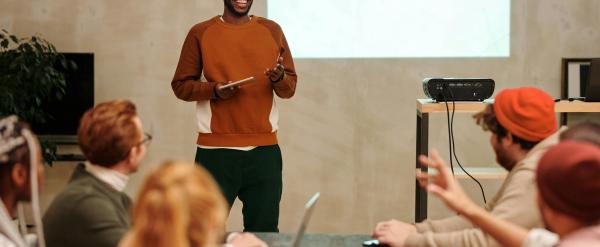 Man presenting to a group in a meeting room with a projector screen behind him.