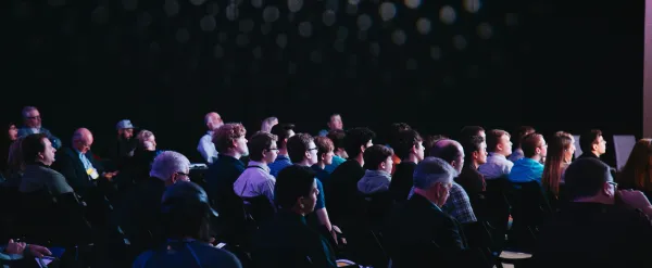 Audience seated in a dimly lit theater with spotlights on the wall.