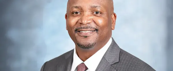 Smiling man in a gray suit and tie with a light blue background.