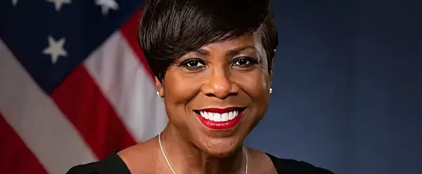 Woman smiling in front of a U.S. flag with a dark background.