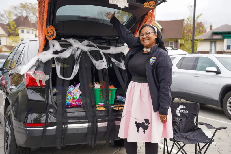 Woman smiling next to a decorated car trunk filled with Halloween treats.