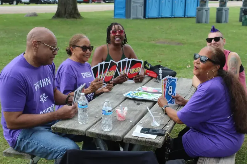 Five people sitting at a picnic table outdoors playing UNO and smiling.
