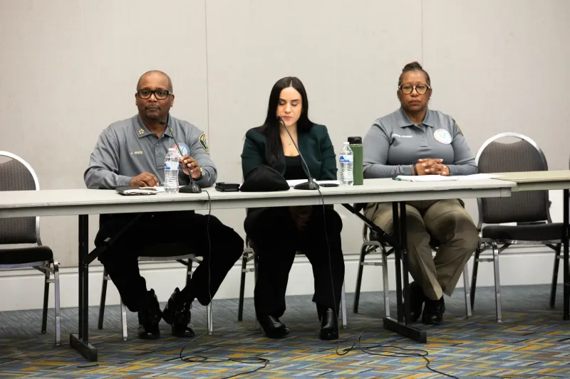 Three people sitting behind a table at a panel discussion in a conference room.