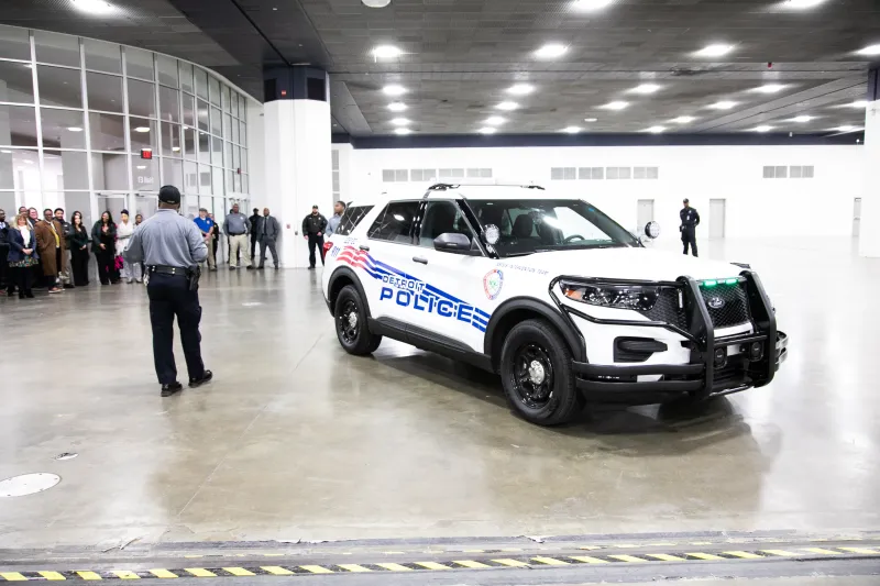 Police SUV parked indoors near a group of people and a standing officer.