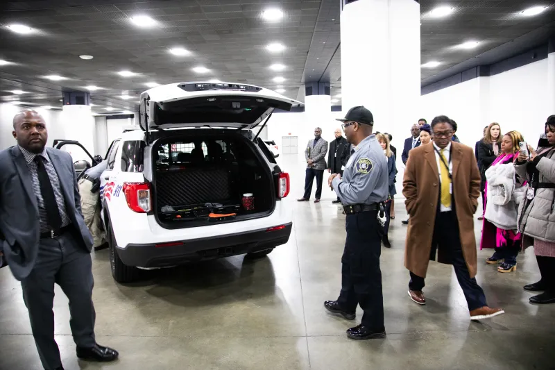 Police SUV with open trunk indoors, people and officers standing nearby.