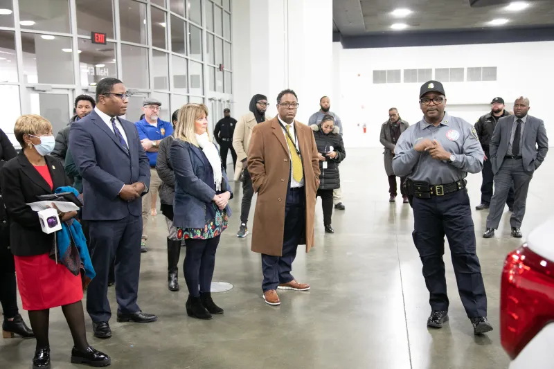 People listening attentively to a uniformed speaker in a spacious indoor setting.