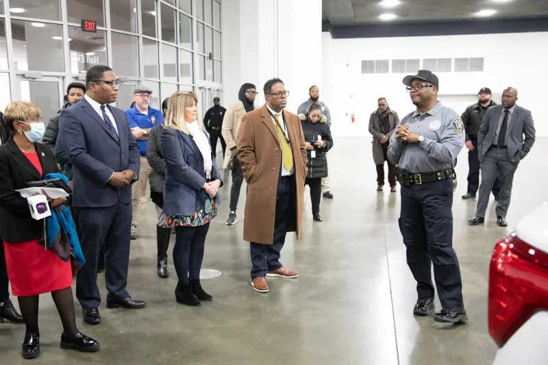 A group of people listens to a man speaking in an indoor, modern, industrial setting.