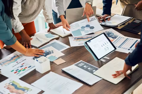 People collaborating over charts, graphs, and a tablet at a conference table.