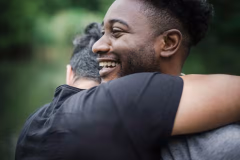 Two people hugging outdoors, one smiling brightly.