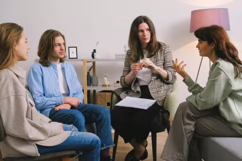 Four people sit in a circle having a group discussion in a cozy room.