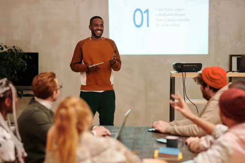 Man presenting to a group in a meeting room with a projector screen behind him.