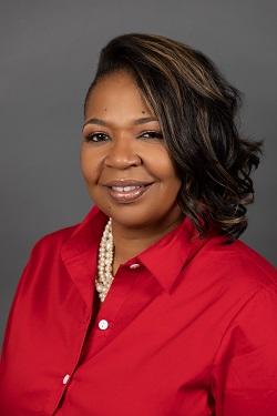 Smiling woman in a red shirt with pearl necklace against gray background.