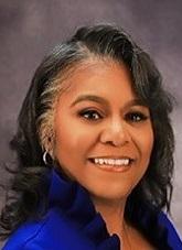 Smiling woman with dark wavy hair, wearing a blue top, against a gray background.