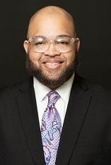 Man in a suit and tie smiling against a black background.